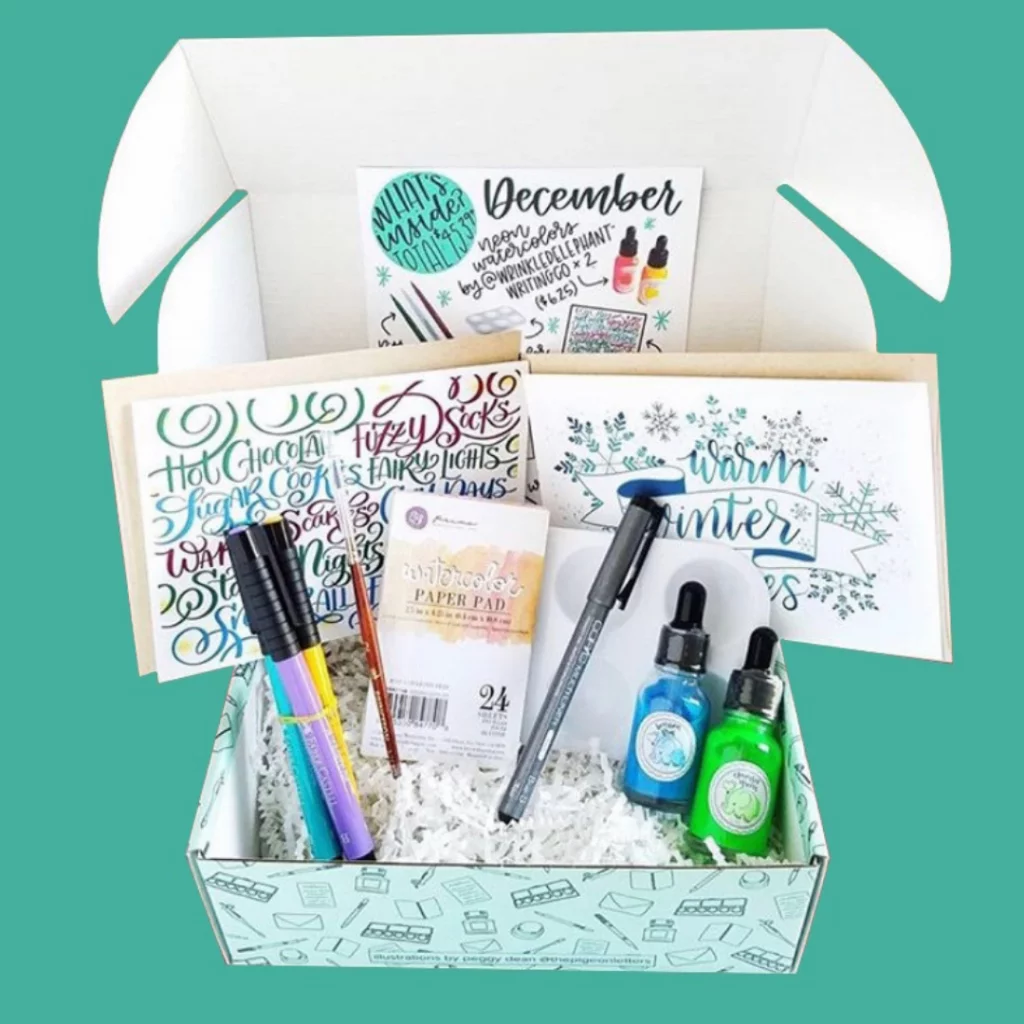 Art subscription box containing lettering guides, pens and ink bottles.